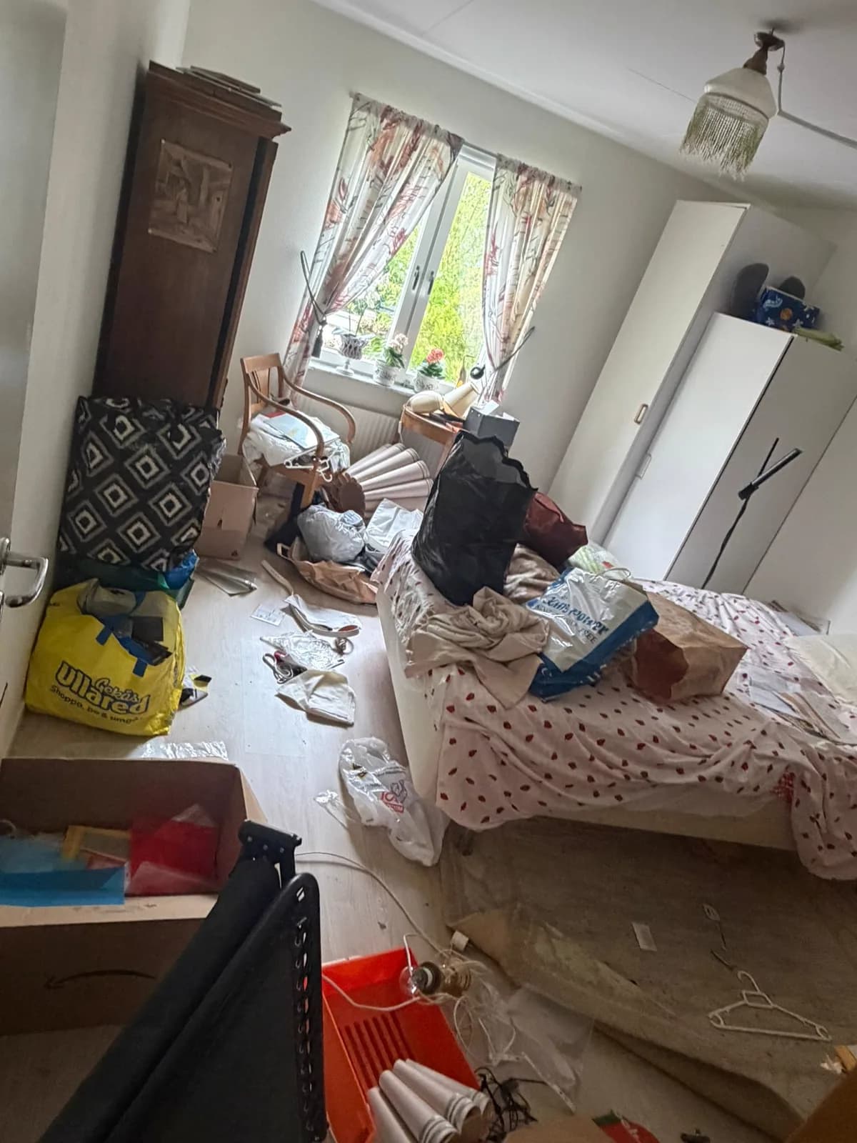 Sovrum före arbetet med föremål och påsar över golv och säng